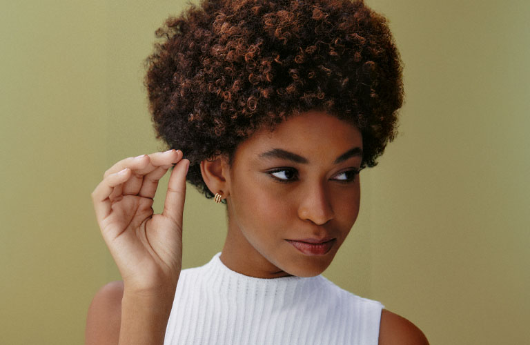 Foto de una mujer con cabello corto y rizado. El fondo tiene tonos verdes y amarillos, y lleva una blusa roja con mangas abullonadas.